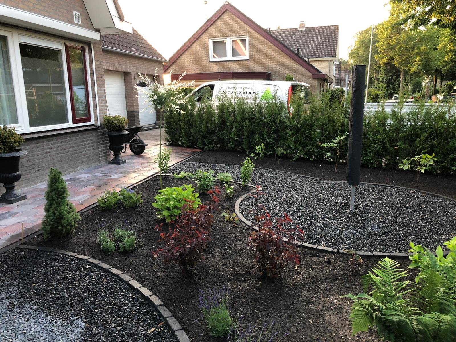 Aangelegde voortuin met borders, jonge beplanting en terraspotten