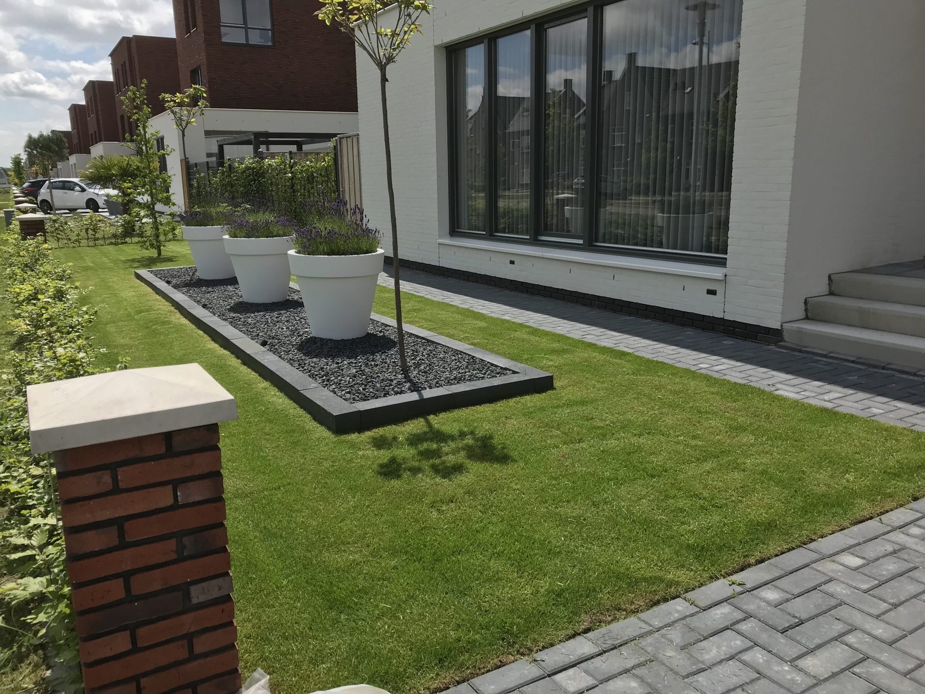 Strak aangelegd gazon met bestrating en plantenbakken langs een moderne woning